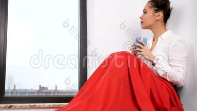 一个女人坐在一扇大窗户旁边，身披<strong>红毯</strong>
